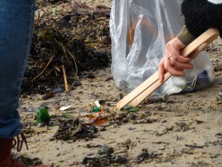 Mit einer Zange wird Müll vom Strand aufgesammelt.