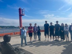Die Gruppe der Gedenkstättenfahrt steht am Hafen in Gdynia. Eine Reiseleiterin erklärt etwas.