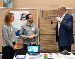 Drei Personen stehe in einem Gespräch nebeneinander. Zwei der Personen werden von einer Mikrofon haltenden Person interviewt.