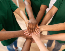 Zu sehen sind mehrere Arme verschiedener Menschen. Die Menschen reichen ihre Hänge in die Mitte und legen sie übereinander. Dabei stehen die Personen im Kreis.