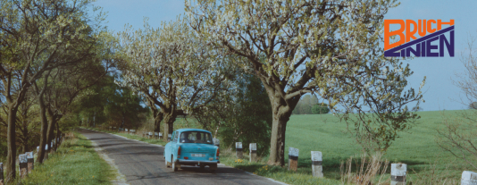 Ein blauer Trabbi föhrt auf einer Landstraße.