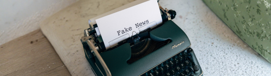 Aus einer Schreibmaschine kommt ein Papier, auf dem Fake News steht.