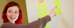 Eine Person zeigt auf einer Pinnwand auf Post-its.