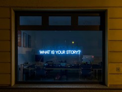 In einem Fenster steht mit Neonschrift: What's your story?