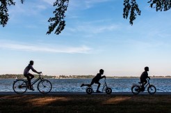 An einem Ufer fahren 3 Personen Fahrrad. Ihre Umrisse sieht man nur als Schatten.